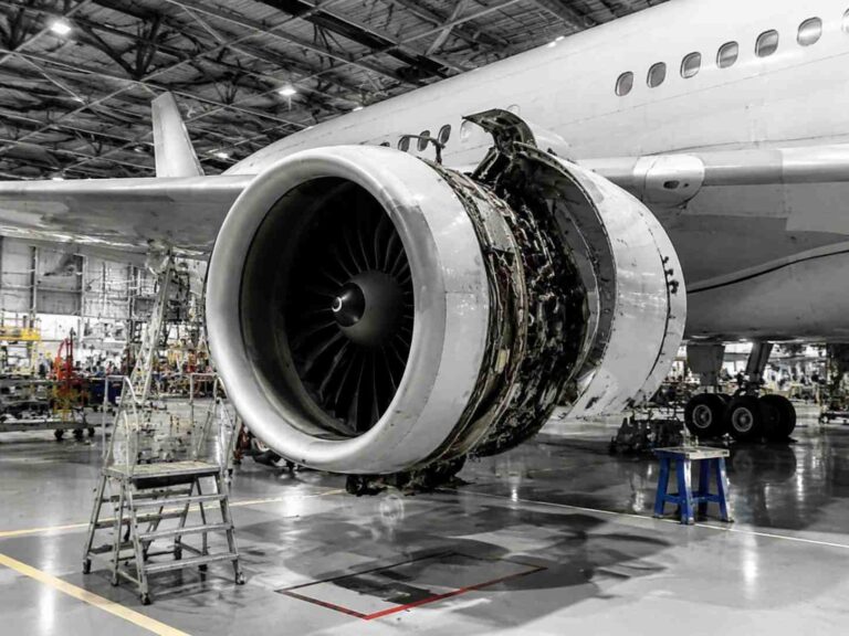 Jet engine under maintenance in a hangar, with exposed turbine and repair scaffolding nearby.
