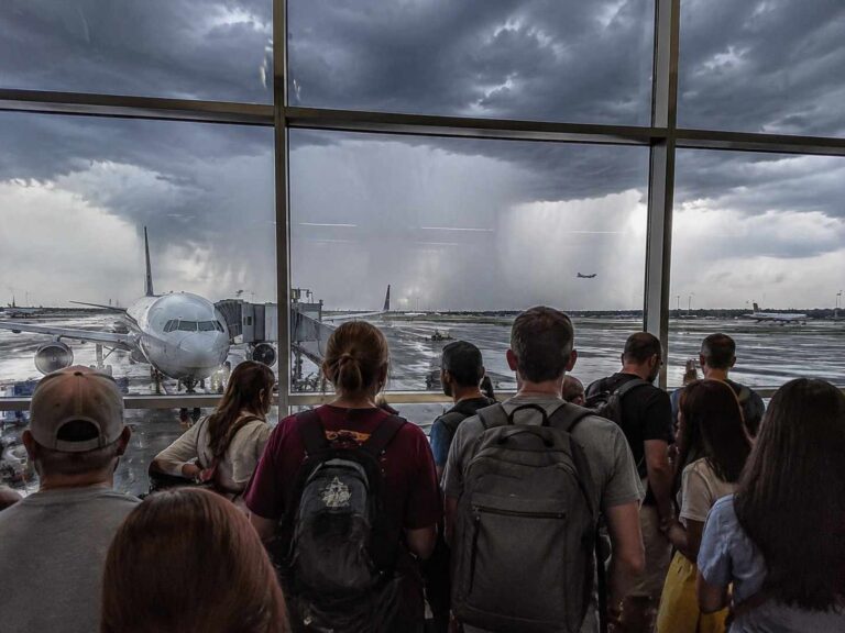 Passengers stand at a terminal window watching a large airplane dock at the gate as dark storm clouds roll in.