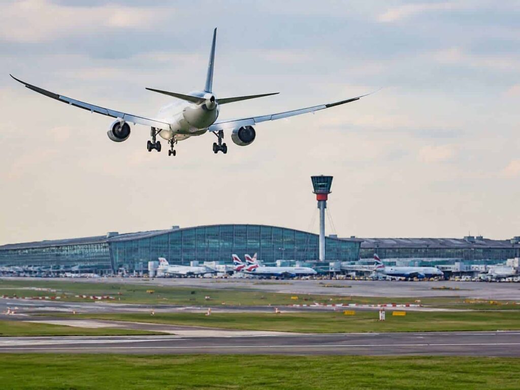 Airliner descending toward the runway with a large terminal and control tower in the background.