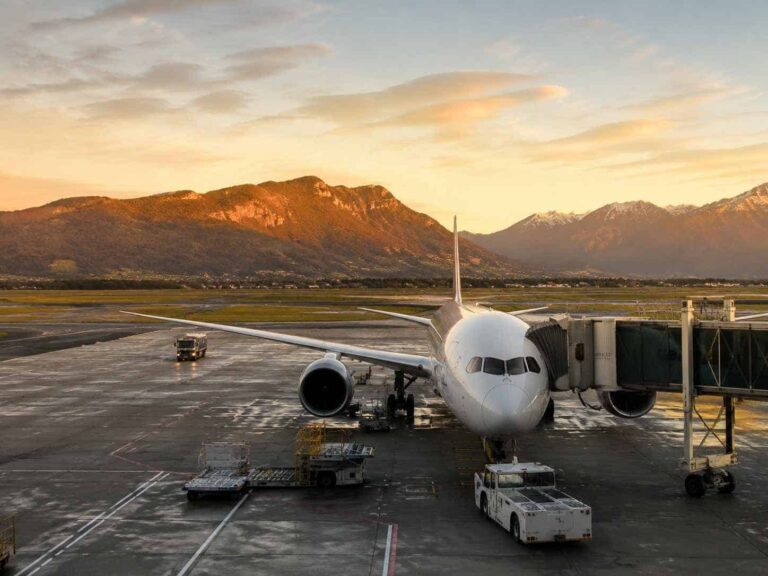 Front view of a passenger plane at a gate during sunset, with mountains in the distance on the horizon.