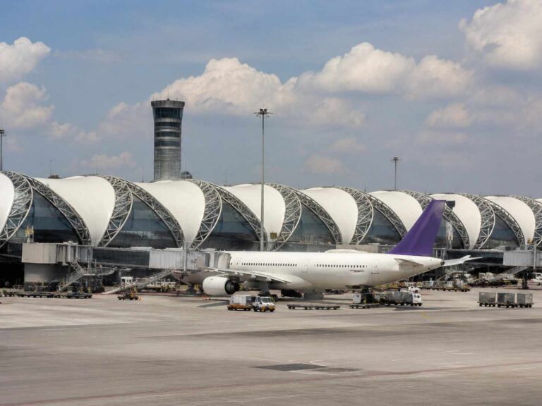 Passenger jet at a gate beside a curved white-roofed concourse, purple-tailed aircraft ready for boarding.