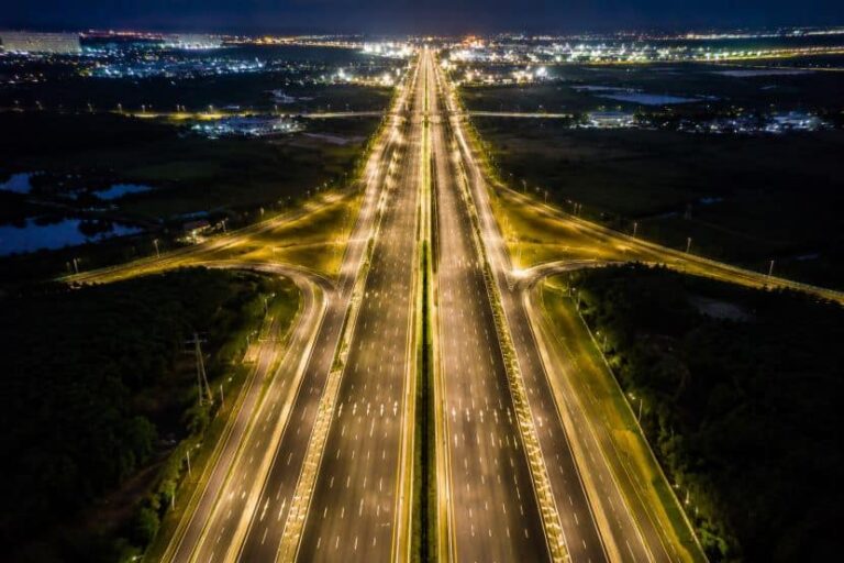 Aerial night view of a long, divided highway with bright streetlights and a central median stretching to the horizon.