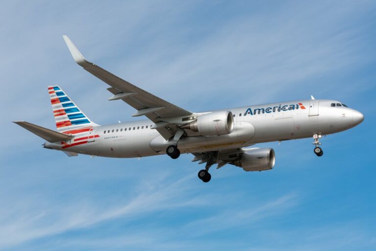 American Airlines jet in flight against a clear blue sky, landing gear extended and flaps down for landing.