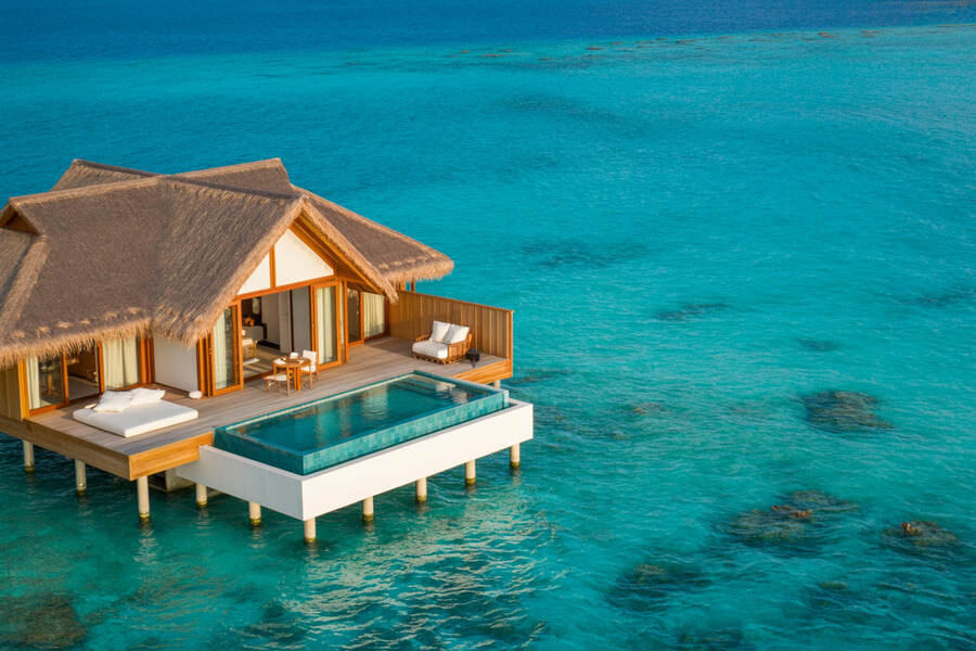 Overwater bungalow with a thatched roof and a private deck extending over clear turquoise water.