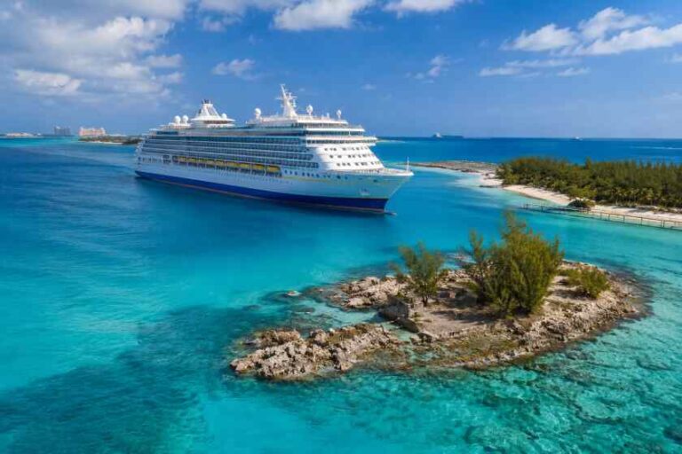 Cruise ship anchored beside a small rocky island with green shrubs in turquoise water.