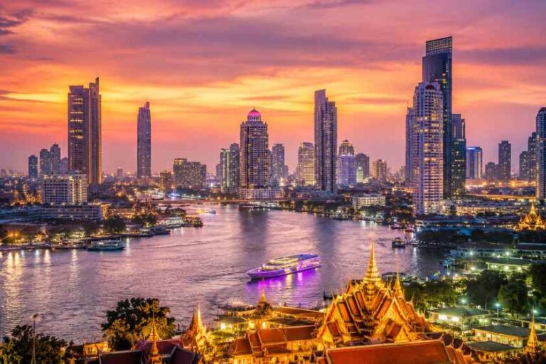 Sunset over a city skyline with a river and illuminated temples in the foreground, Bangkok-style cityscape glowing with orange and purple hues