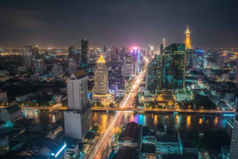 Nighttime cityscape of a illuminated downtown with a river, tall skyscrapers, and glowing streets.