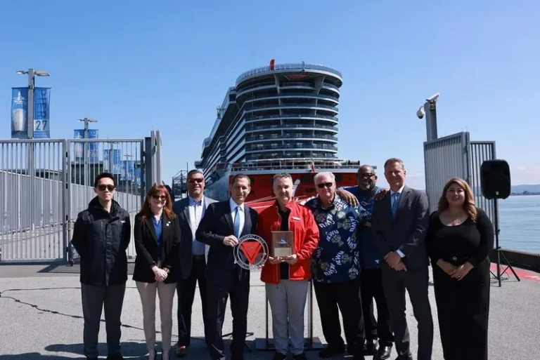 Ten people stand together on a dock, posing with awards in front of a large cruise ship on a sunny day.