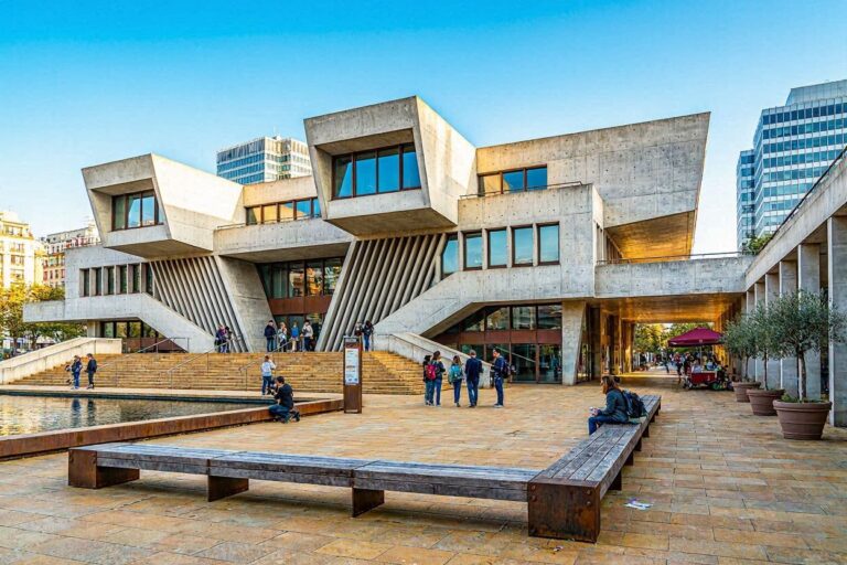Bold, angular concrete building with stepped entrances and a wide public plaza where people sit and chat.