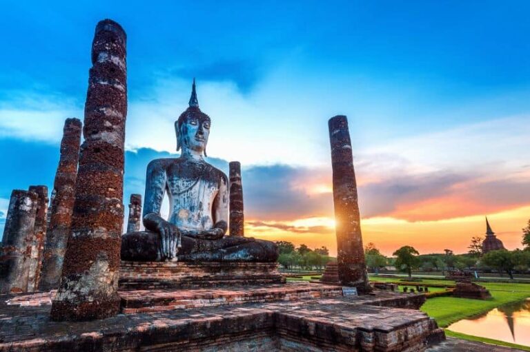 Seated ancient Buddha statue among weathered brick columns at sunset in a historic temple complex.
