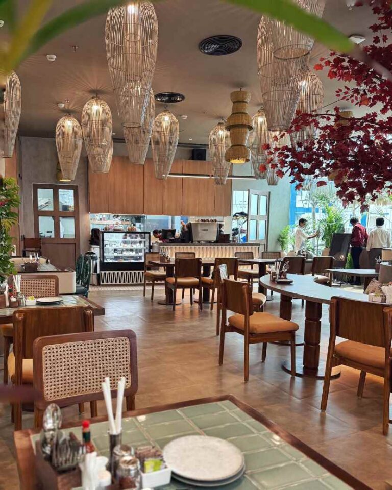 Restaurant dining area with wooden tables and brown chairs, large hanging wicker lanterns, and a service counter in the back.
