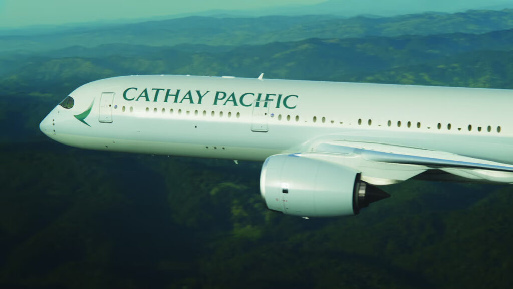 Side view of a Cathay Pacific commercial airliner in flight over a green landscape.