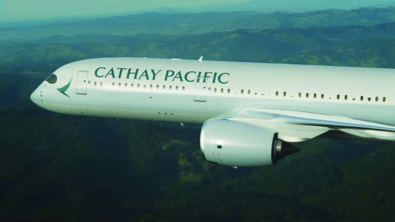 Side view of a Cathay Pacific commercial airliner in flight over a green landscape.