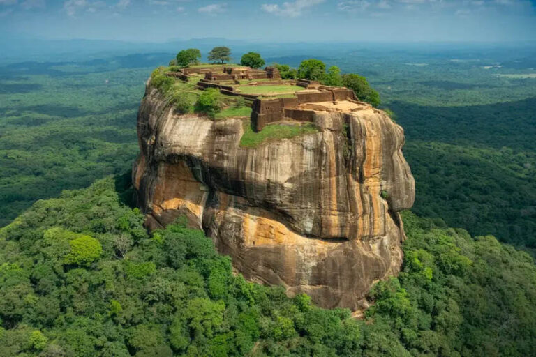 Massive flat-topped rock with ancient terraces and a few trees on top, rising above dense tropical forest.