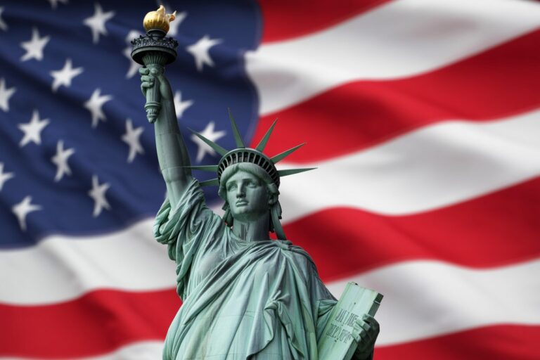 Statue of Liberty holding its torch with a waving American flag in the background