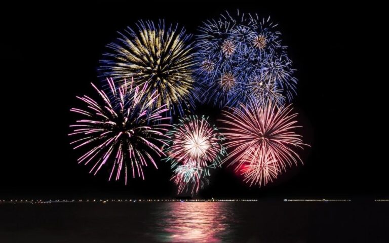 Colorful fireworks exploding over a dark lake at night, with reflections on the water.