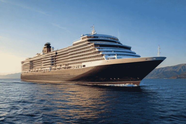 Massive cruise ship with many decks sailing on calm blue sea with distant mountains.