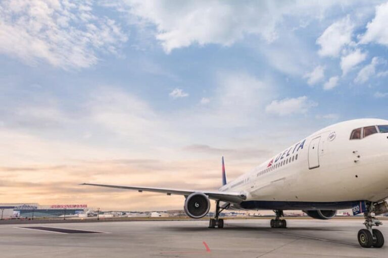 Delta airliner parked on the airport tarmac at sunset with a blue sky behind it.