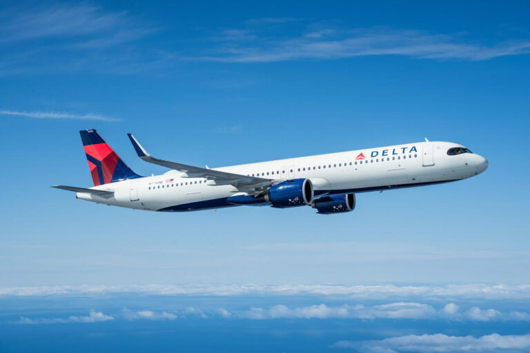 Delta Air Lines airplane in flight over a blue sky, white fuselage, blue engine nacelles, and red/blue tail logo visible. Delta jet cruising above clouds with winglets and engine nacelles visible.