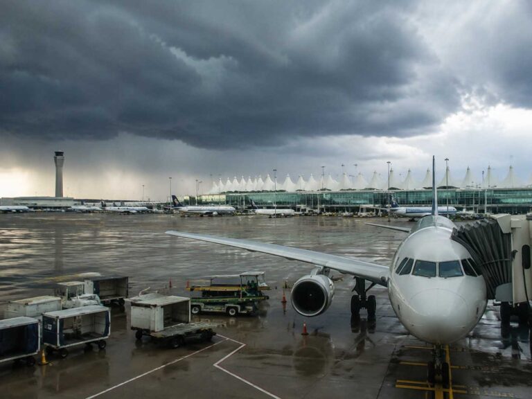 Airplane at gate with jet bridge under dark stormy clouds and rain-soaked tarmac.