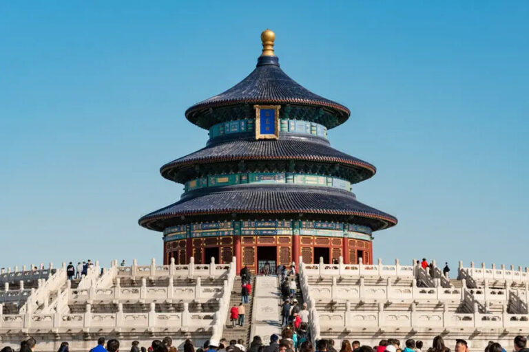 Temple of Heaven in Beijing: a three-tiered blue-tloing circular roofed temple atop a white marble terrace with visitors walking the stairs up to it.