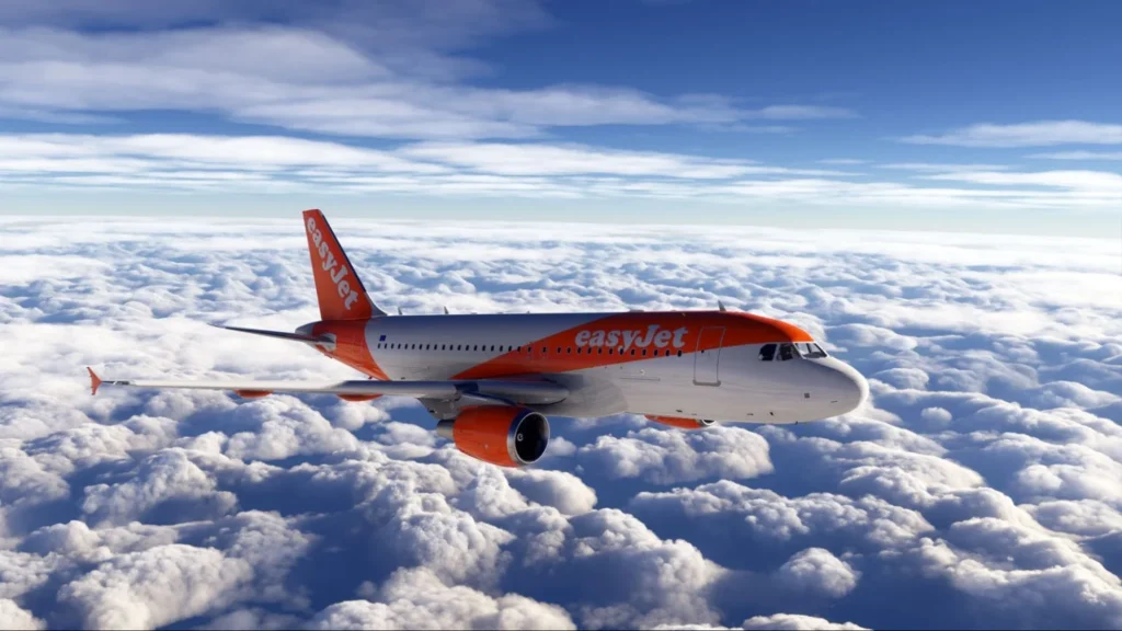 EasyJet plane flying above white clouds with blue sky, side view of orange and white jet in flight