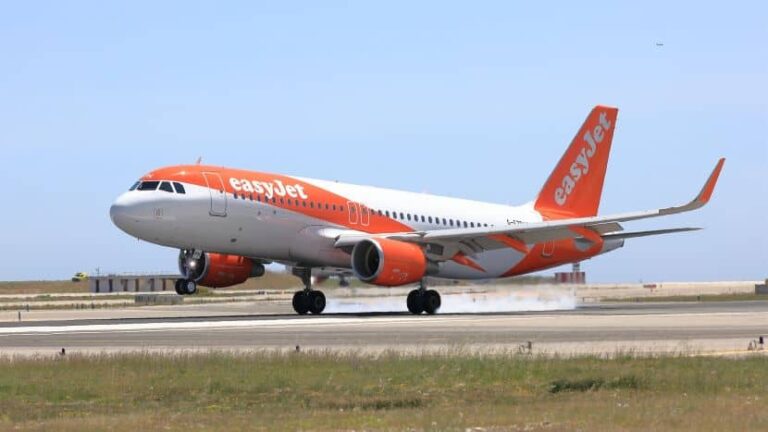 Orange-and-white easyJet airplane touching down on runway with smoke from wheels.