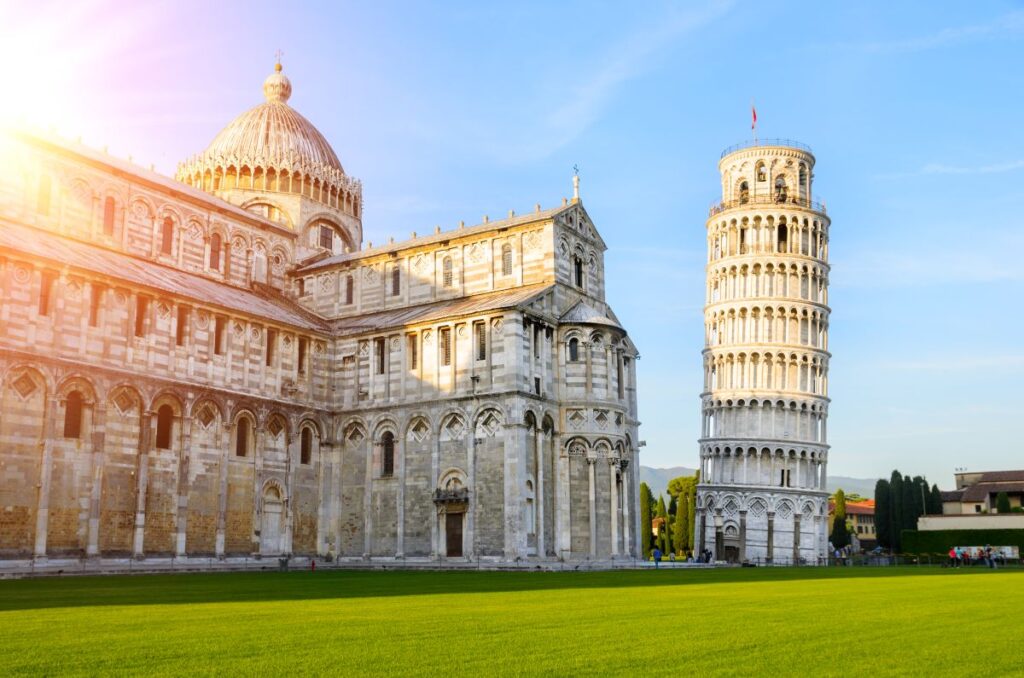 Cathedral of Pisa and the Leaning Tower of Pisa on a sunny day with a green lawn.