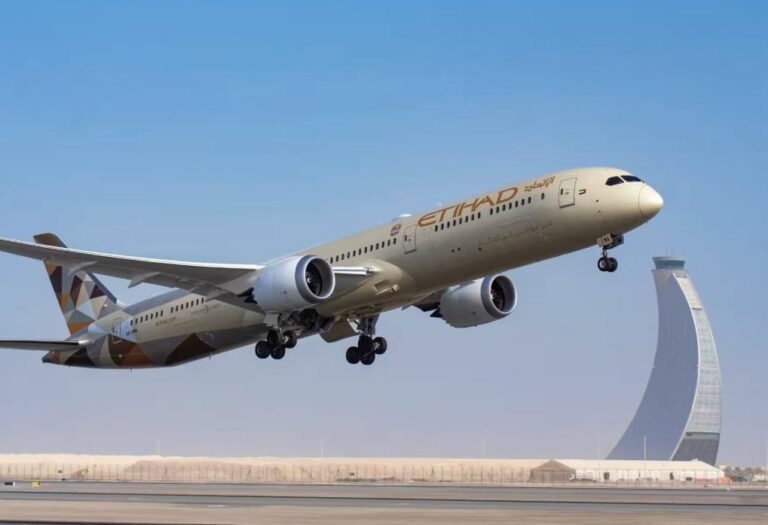 Etihad Airways jet lifting off from a runway, landing gear down, with a curved modern tower in the background against a blue sky.
