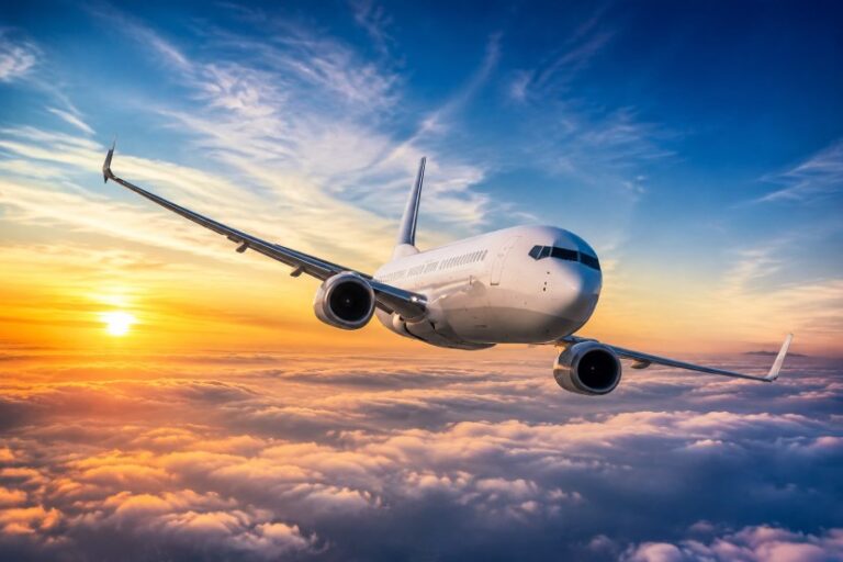 Commercial airplane flying above orange clouds during sunset with blue sky overhead