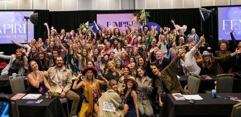 Large diverse group of attendees posing for a group photo at a conference, with lanyards and event banners in the background.