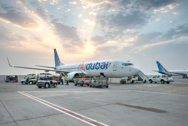 Flydubai airplane on the tarmac being serviced by ground crew and luggage carts at sunset