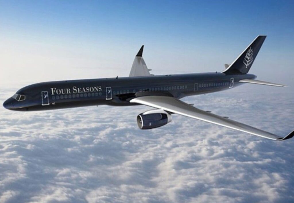 Commercial jet painted in Four Seasons livery flying above cloudy sky.