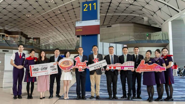 Group of airline staff in uniform posing with promotional signs at an airport terminal near gate 211, smiling for the photo.