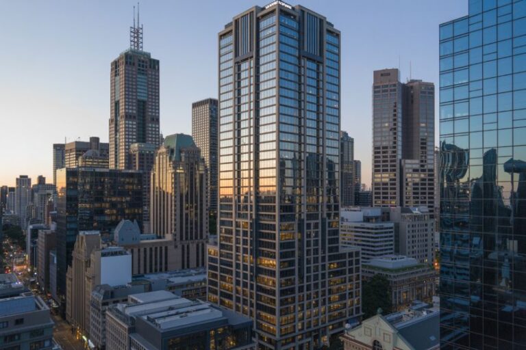 City skyline with tall glass office buildings at sunset, warm light reflecting off windows.