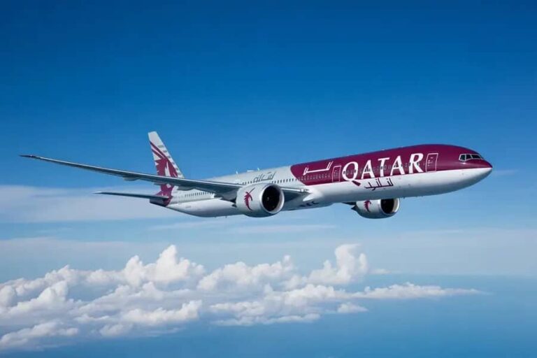 Qatar Airways passenger jet in midflight above fluffy white clouds with a blue sky.