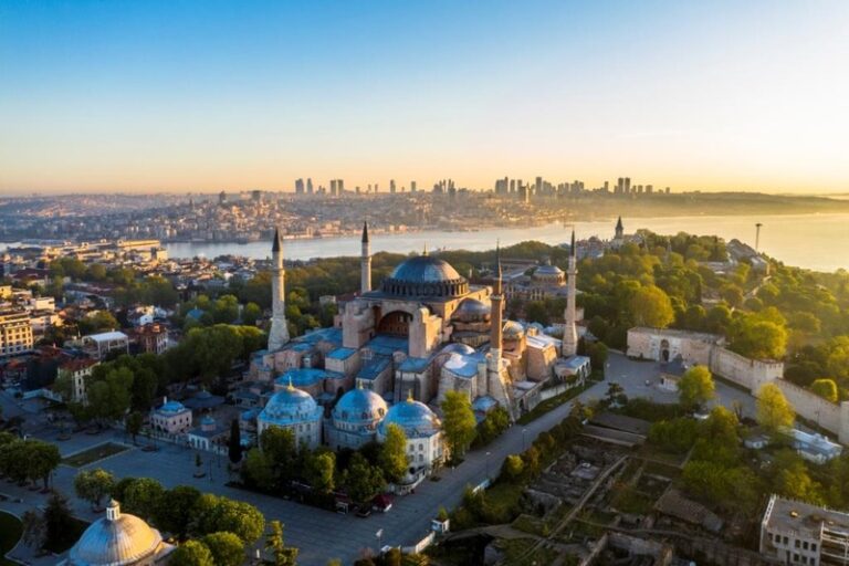 Aerial view of Hagia Sophia with domes and four minarets in Istanbul at sunset over the city contrast with a river in the distance and a blue sky.