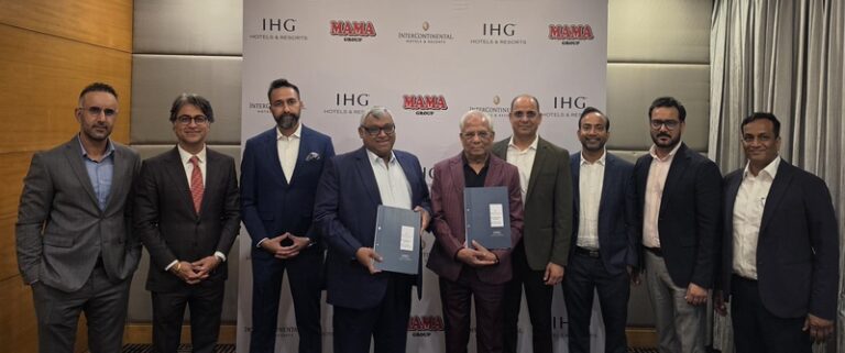 Group of ten men in suits posing for a photo at a signing event, with two men in front holding blue folders; backdrop shows MAMA Group and IHG logos.