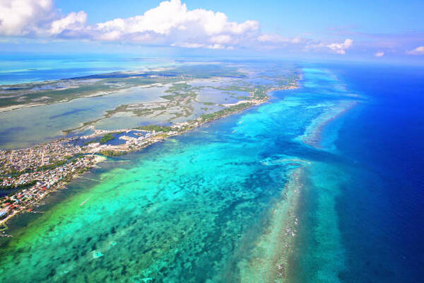 Aerial view of a tropical coastline with turquoise lagoons, coral reef, and a small town along the shore.