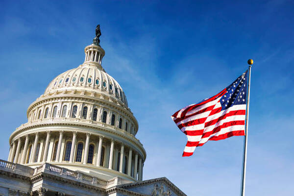 U.S. Capitol dome with a waving American flag against a blue sky