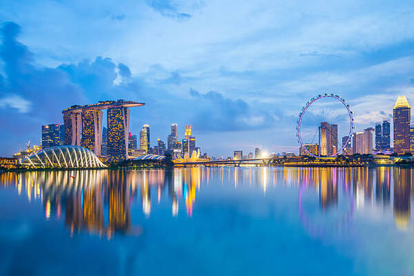 Singapore skyline at dusk with illuminated Marina Bay Sands, ArtScience Museum, and Singapore Flyer reflecting on the bay's calm water.