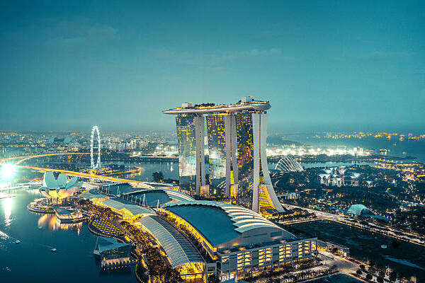Nighttime aerial view of Singapore featuring Marina Bay Sands hotel, waterfront promenade, and the Singapore Flyer.