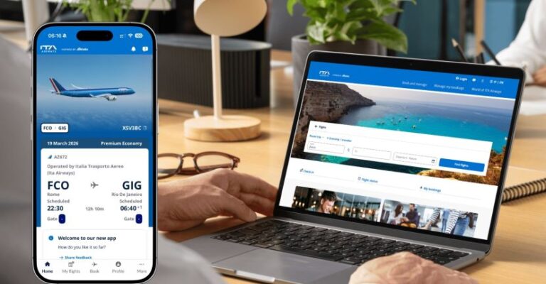Phone shows an ITA Airways flight ticket while a laptop displays a travel booking site on a desk.