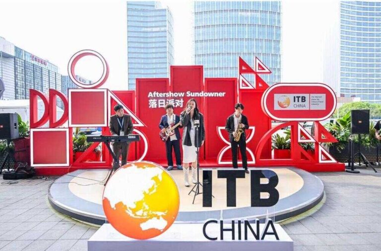 Band performing on a red geometric stage at ITB China, with a large globe prop in the foreground and city buildings behind.