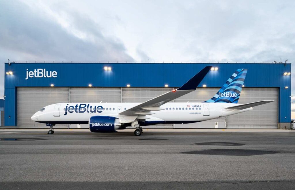 JetBlue narrow-body aircraft parked in front of a blue hangar with JetBlue branding on the fuselage and tail.