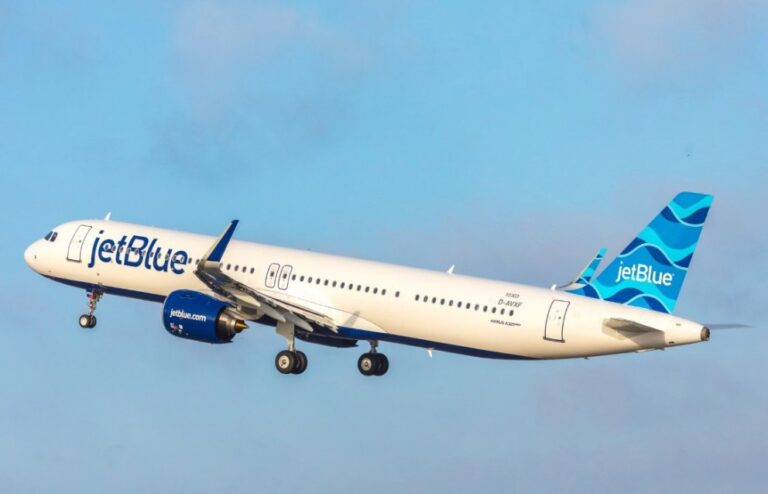 JetBlue passenger jet in flight, white fuselage with blue branding and blue tail against a clear sky.