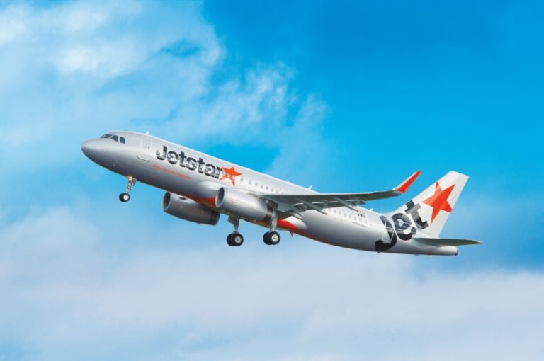 Jetstar commercial airplane taking off into a blue sky, with red star logo on tail and landing gear extended.