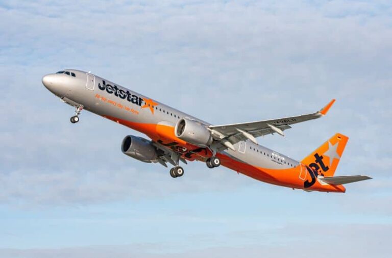 Jetstar airliner ascending after takeoff, orange and gray livery against a blue sky.