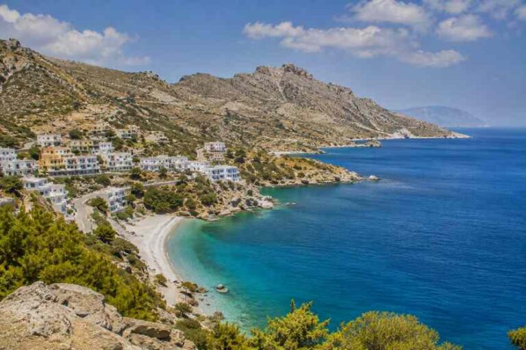 Coastal village with white houses perched on a rocky hillside above a turquoise bay and curved sandy beach. Reviewing the sea and cliffs.