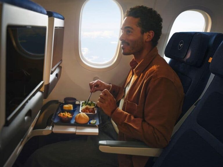 A man seated on an airplane eating a meal from a tray on the fold-out table beside a window.